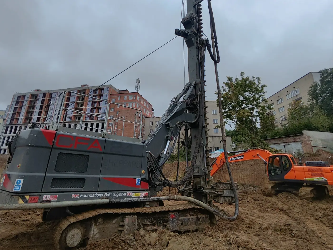 Бурова установка Mait CFA 24 й екскаватор Develon на будмайданчику в місті